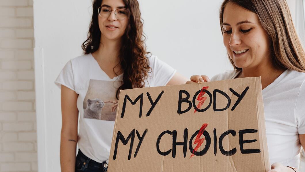 Twee vrouwen in witte shirts, één houdt een bord vast waar 'my body my choice' op staat. 