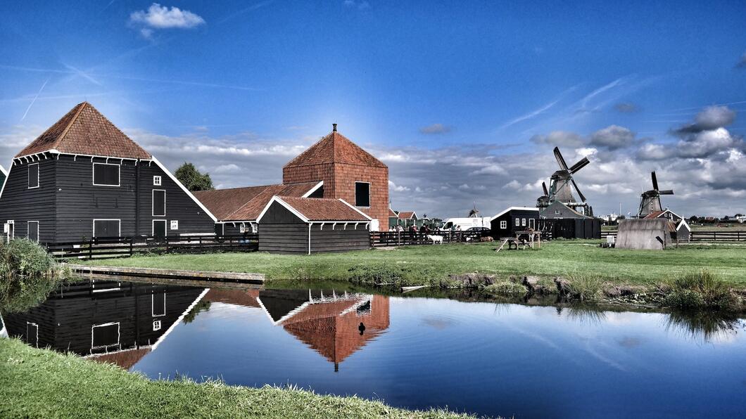 Nederlands landschap waarop een riviertje te zien is wat door een weiland loopt, met daarop molens en boerderijen.